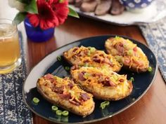 three loaded baked potatoes on a black plate next to a glass of beer and flowers