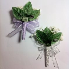 two green and white flowers with ribbons attached to each other on a white table top