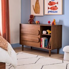 a child's bedroom with blue walls and artwork on the wall, along with a wooden dresser