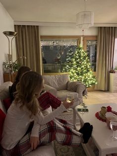 a woman sitting on top of a couch next to a christmas tree in a living room