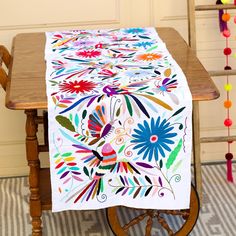 a wooden table topped with a white table cloth covered in multicolored floral designs