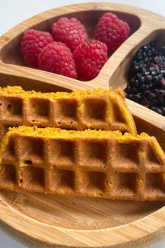 two waffles on a wooden plate with raspberries and blueberries in the background