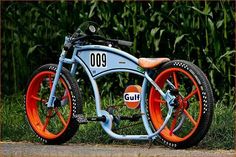 an orange and blue motorcycle parked on the side of a road next to tall grass