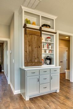 a kitchen with white cabinets and wood flooring in the middle of an open living room