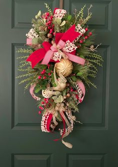 a christmas wreath hanging on the front door with red ribbon and bells attached to it