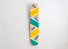 a skateboard is hanging on the wall and it's painted yellow, green, blue, and white