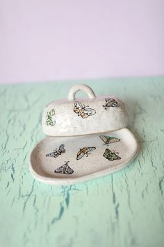 two ceramic dishes with butterflies on them sitting on a blue tableclothed countertop