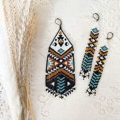 two pairs of beaded earrings sitting on top of a white table next to a plant