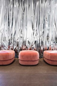 three pink chairs sitting next to each other in front of silver foil covering the walls