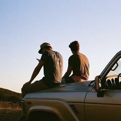 two men are sitting on the hood of a pick up truck looking at something in the distance