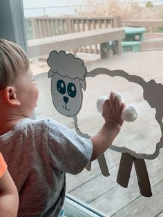 a young boy looking at a paper cut out of a sheep on a window sill