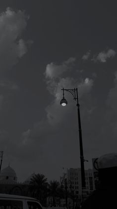 a black and white photo of a street light with clouds in the sky behind it