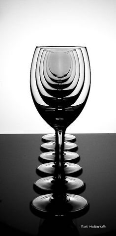 a black and white photo of a wine glass on a table with the reflection of it