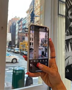 a woman is holding up her cell phone to take a selfie in the city