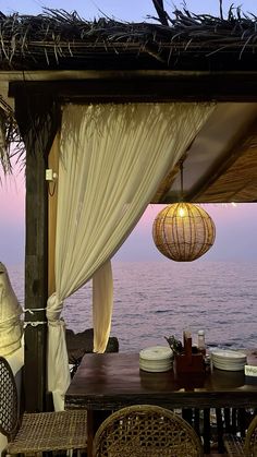 an outdoor dining area with wicker chairs and tables overlooking the ocean at sunset or dawn