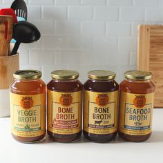 four jars of bone broth sit on a counter next to utensils and spoons