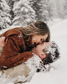 a man and woman are laying in the snow with their noses close to each other