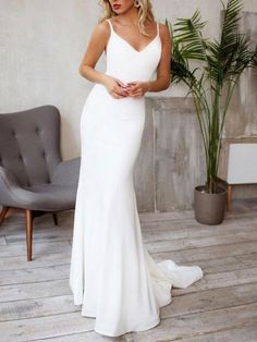 a woman wearing a white dress standing in front of a chair and potted plant