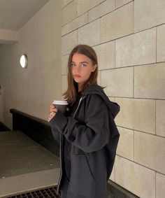 a woman holding a coffee cup standing next to a wall