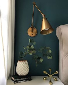 a nightstand with a lamp, potted plant and books on it next to a chair