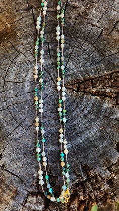 two necklaces with beads are sitting on top of a piece of tree trunk in the woods