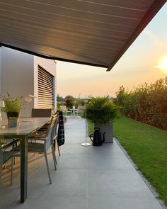 the sun is setting on an outdoor patio with table, chairs and potted plants