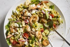 a white plate topped with salad and shrimp on top of a marble countertop next to a fork