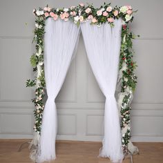 a white wedding arch decorated with flowers and greenery on the floor in front of a wall