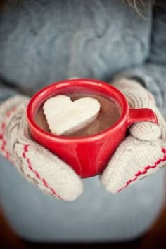 a woman holding a cup of hot chocolate with marshmallows in her hands