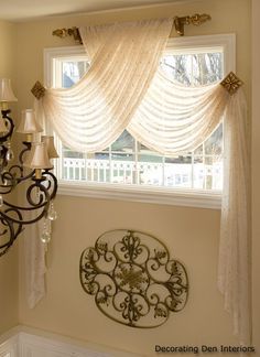 a chandelier hanging from the side of a wall next to a window with sheer curtains