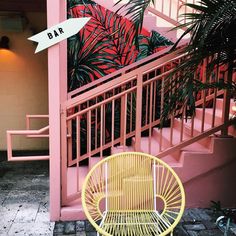 a yellow chair sitting in front of a pink building with palm trees on the balcony