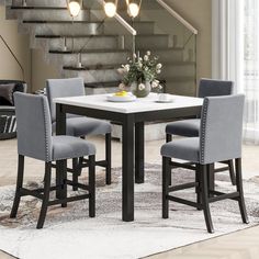 a dining room table with four chairs and a vase on the table in front of stairs