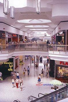 the inside of a mall with people walking around and shops on either side of the escalator