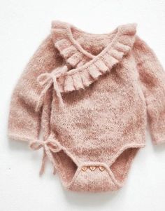 a pink sweater with ruffles on the front and bottom is laying on a white surface