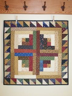 a multicolored quilt hanging on the wall next to coat hooks and pegs