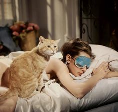 a woman laying in bed with a cat on her lap next to her sleeping mask