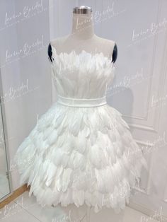 a white dress with feathers on it is displayed in front of a mannequin