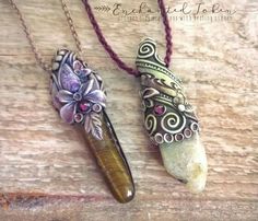 two necklaces with different designs on them sitting on top of a piece of wood