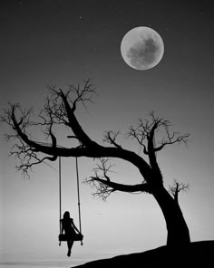 a black and white photo of a person sitting on a swing in front of a tree