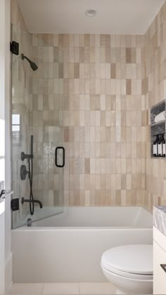 a white toilet sitting next to a bath tub in a bathroom with tiled walls and floor