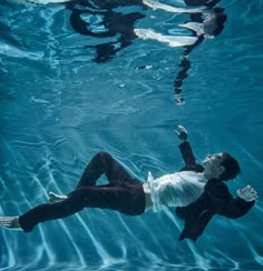 a woman in white shirt and black pants swimming under water