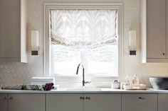 a kitchen with white cabinets and a window covered in roman shades over the windowsill