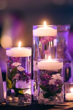 three candles with flowers in them sitting on a table next to some rocks and glass vases