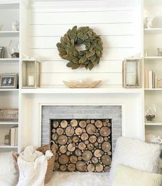 a living room with a fire place and white shelves filled with books, pillows and blankets