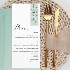 a table setting with place cards and gold utensils on top of a wicker basket