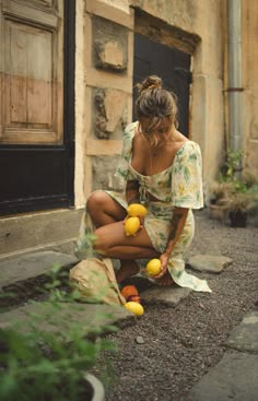 a woman sitting on the ground with lemons in front of an old building,