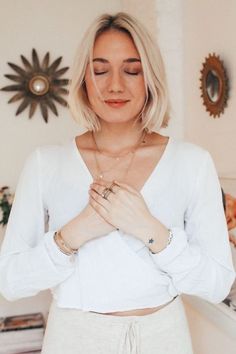 a woman standing in front of a mirror wearing a white shirt and beige pants with her hands together