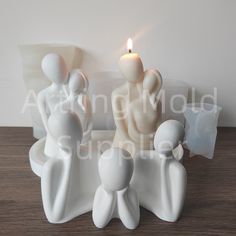 three white ceramic figurines sitting next to a lit candle