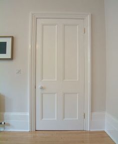 an empty room with a white door and wood flooring on one side, framed artwork on the other