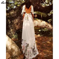 a woman standing in front of a tree wearing a white dress with flowers on it